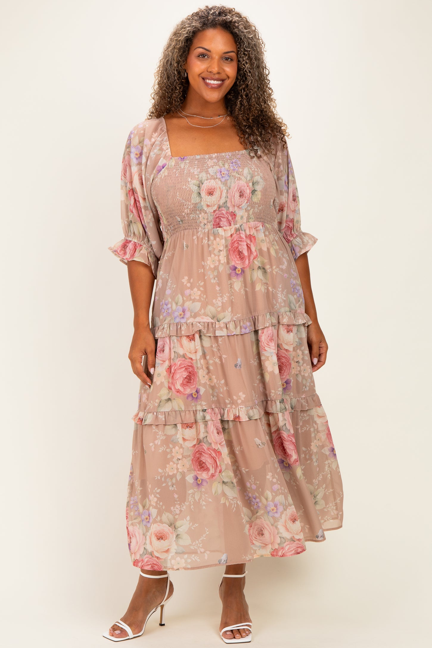 woman wearing a floral plus-size maxi dress with smocked bodice and tiered ruffles, paired with strappy sandals