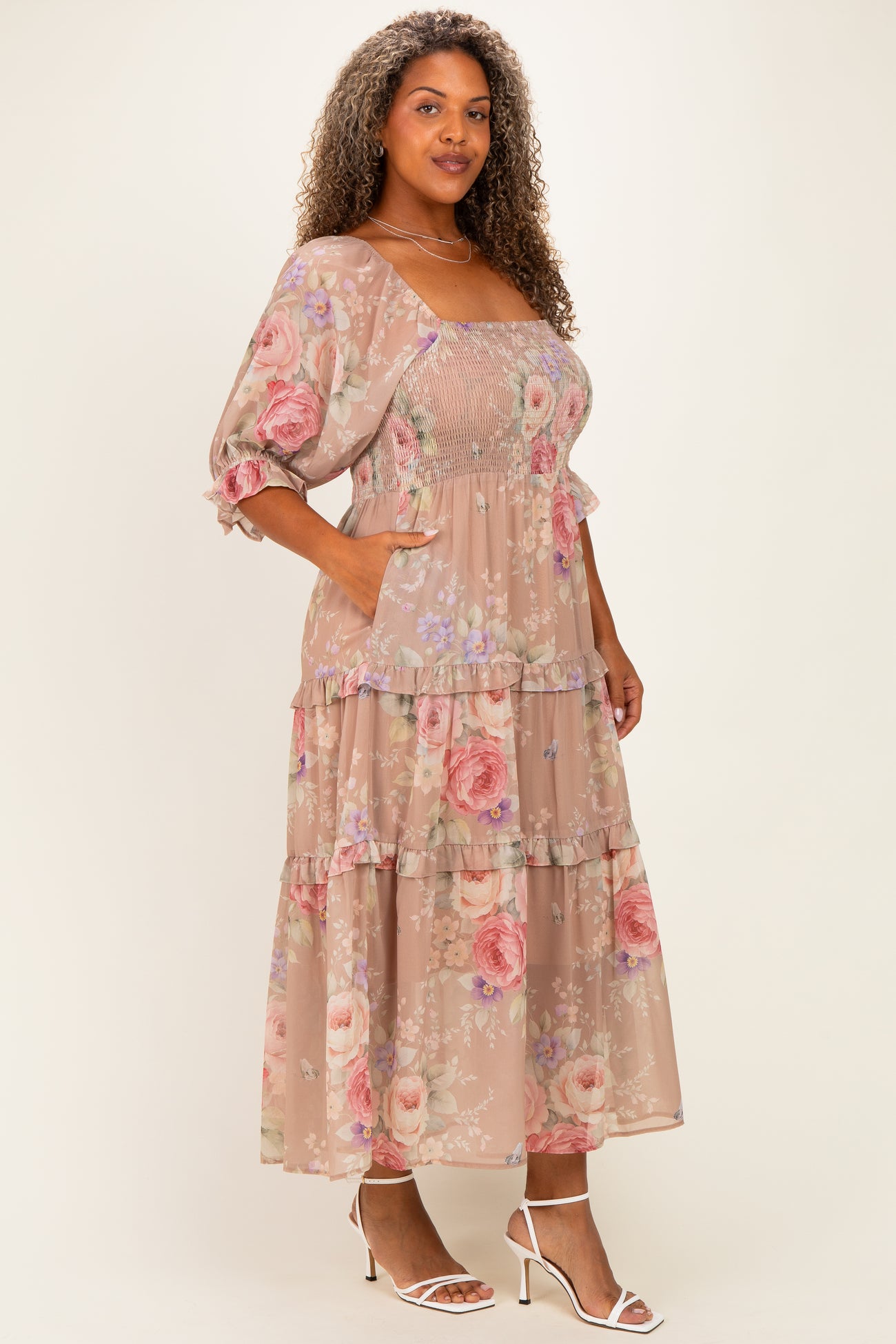 woman wearing a floral plus size maxi dress with puff sleeves and pockets, in soft pastel shades of pink and beige