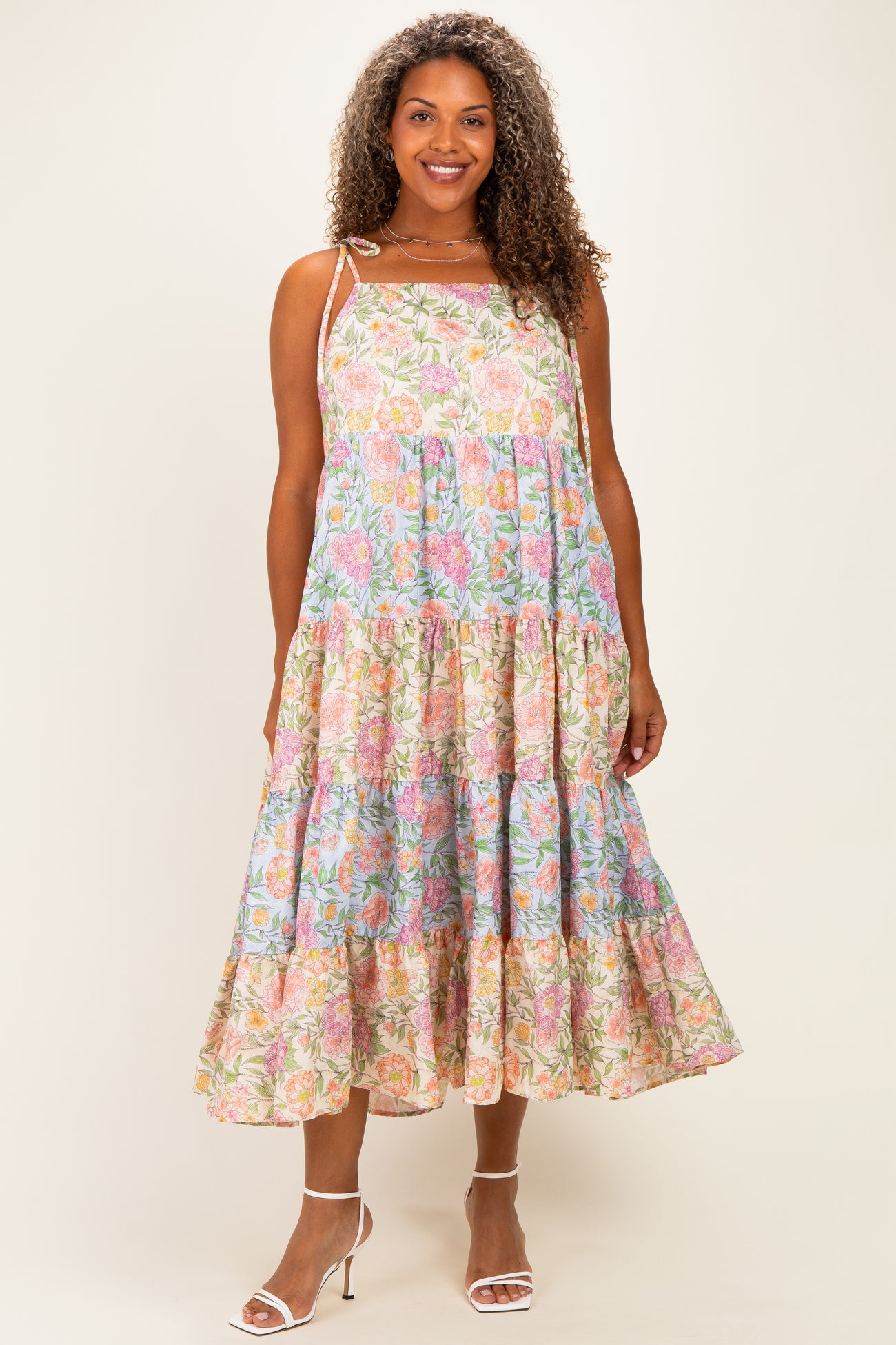 woman wearing a floral midi dress with pink and blue patterns, featuring tiered ruffles and adjustable straps