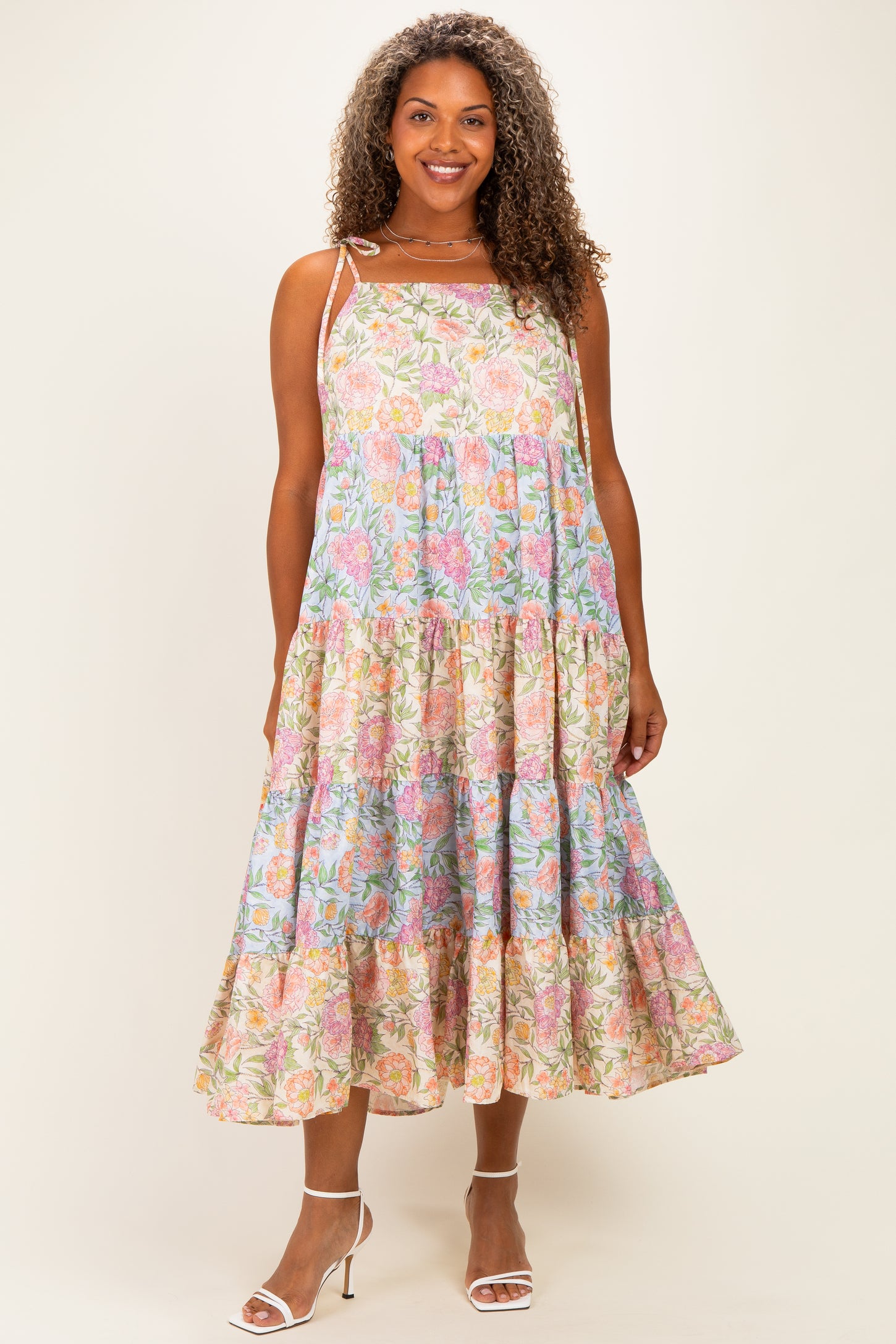 woman wearing a floral midi dress with pink and blue patterns, featuring tiered ruffles and adjustable straps