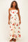 woman wearing a floral print maxi dress with red roses on a cream background, featuring adjustable straps and a flowing silhouette
