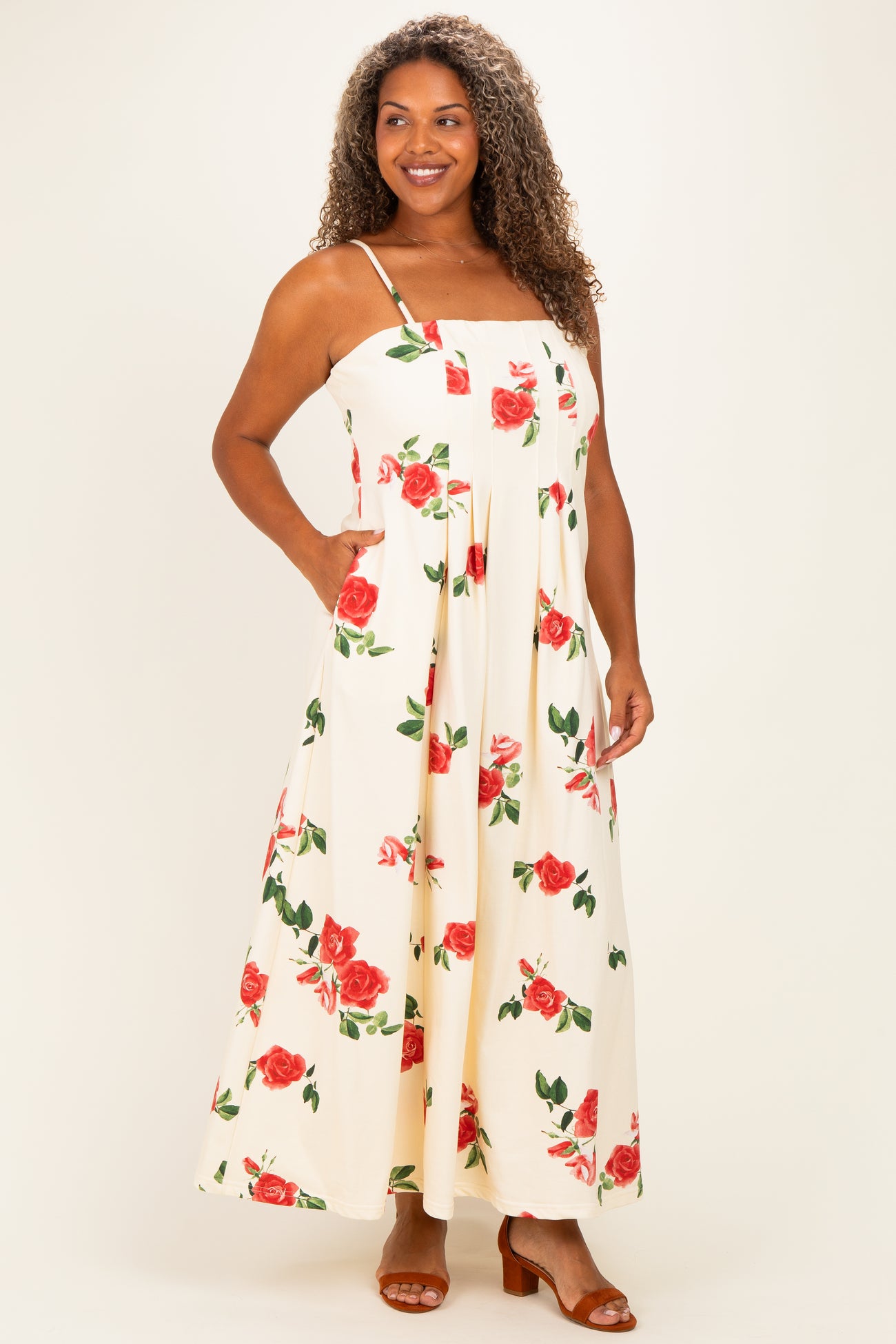 woman wearing a white maxi dress with red floral print and pockets, standing with a slight smile