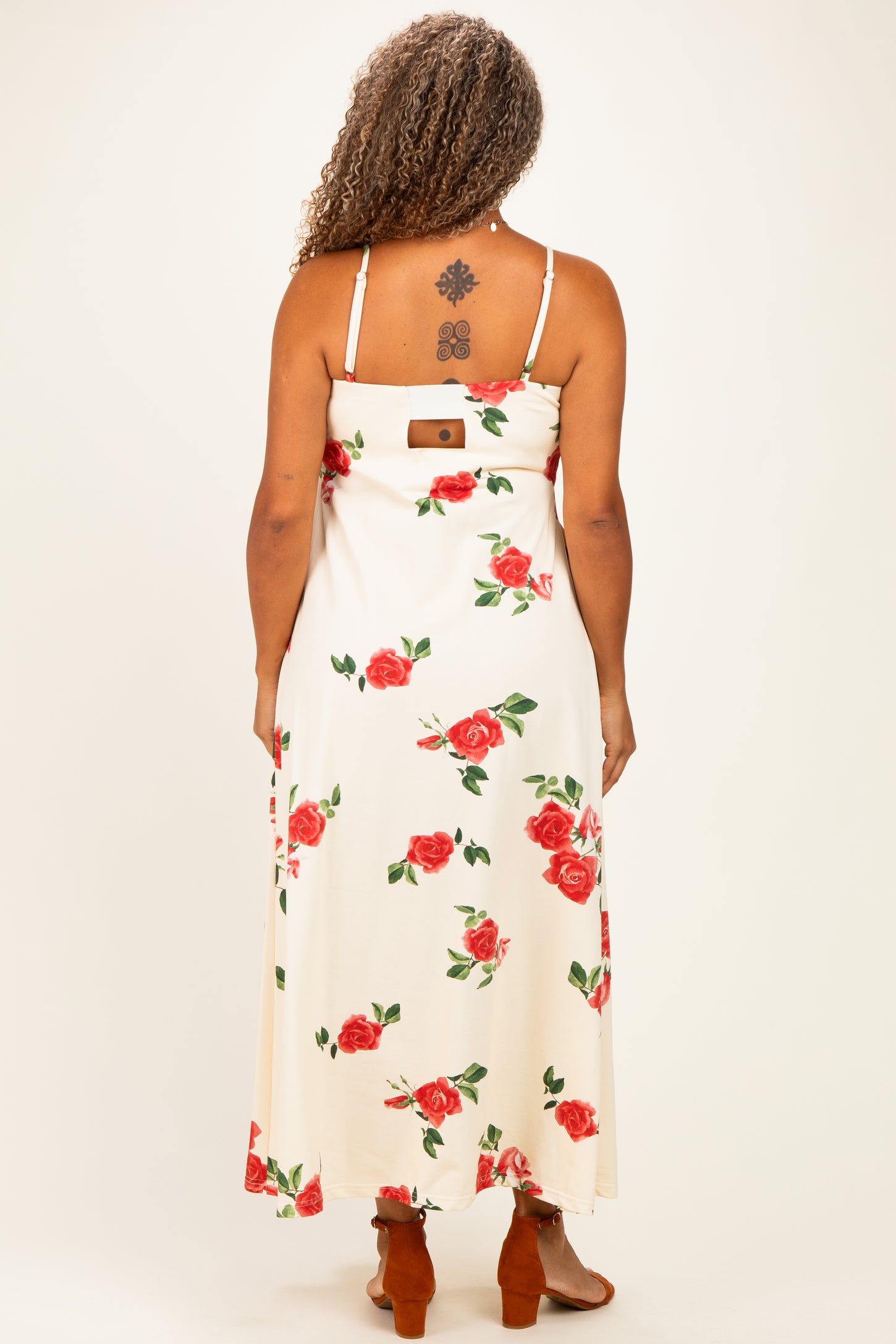 woman wearing a floral maxi dress with a cream background and red roses, showing the back view and strappy design