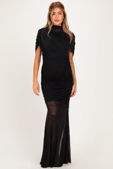 woman wearing a black maternity dress with ruched detailing and a flowing skirt, showcasing her baby bump