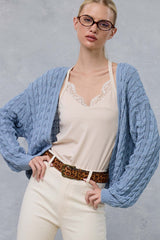 woman wearing a light blue cable knit cardigan over a cream lace camisole and high-waisted cream pants with a leopard print belt