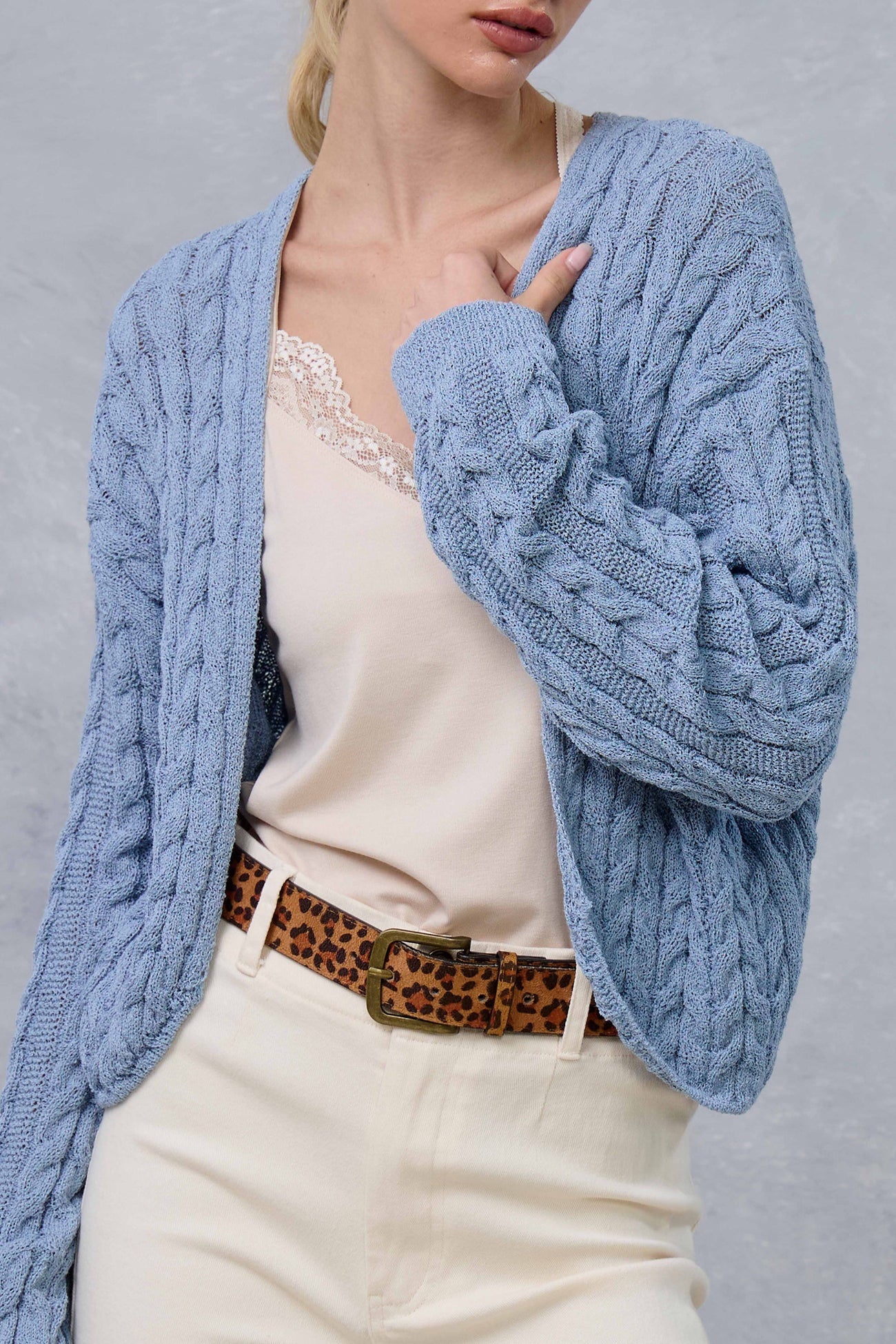 woman wearing a light blue cable-knit cardigan over a beige camisole and styled with a leopard print belt