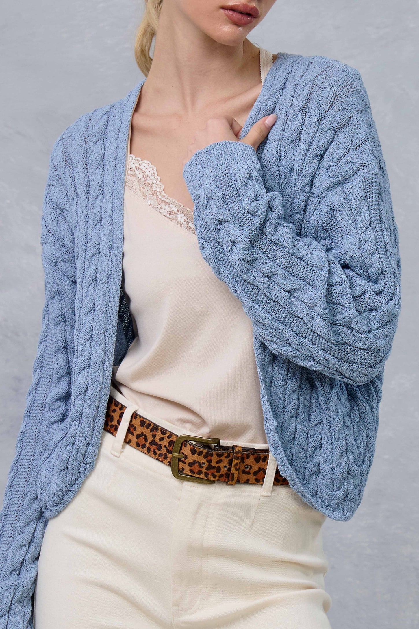 woman wearing a light blue cable-knit cardigan over a beige camisole and styled with a leopard print belt