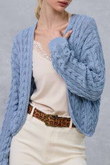 woman wearing a light blue cable-knit cardigan over a beige camisole and styled with a leopard print belt