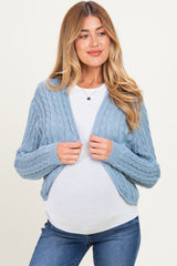 woman wearing a light blue cable knit maternity cardigan over a white top, showing her baby bump while smiling