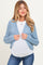 woman wearing a light blue cable knit maternity cardigan over a white top, showing her baby bump while smiling
