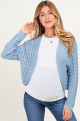 woman wearing a light blue cable knit maternity cardigan over a white top and showing her baby bump