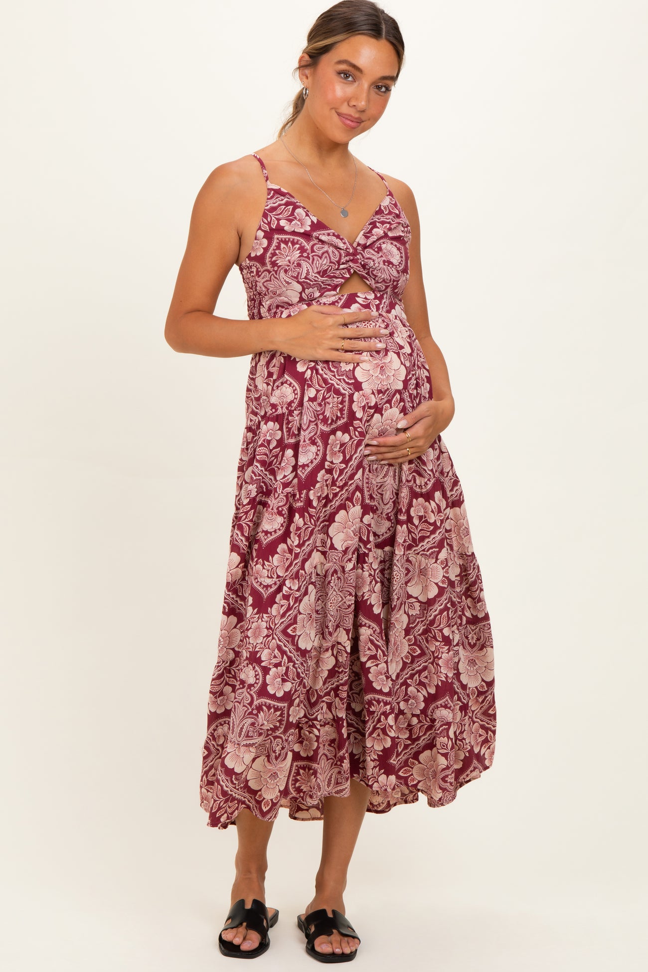 woman wearing a burgundy floral print maternity dress with a cutout detail and holding her baby bump