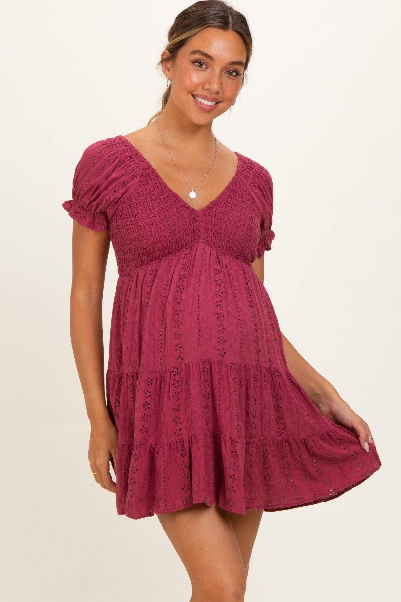 woman wearing a burgundy short sleeve maternity dress with a v-neck and ruffled hem, showcasing her baby bump