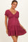 woman wearing a burgundy short sleeve maternity dress with a v-neck and ruffled hem, showcasing her baby bump