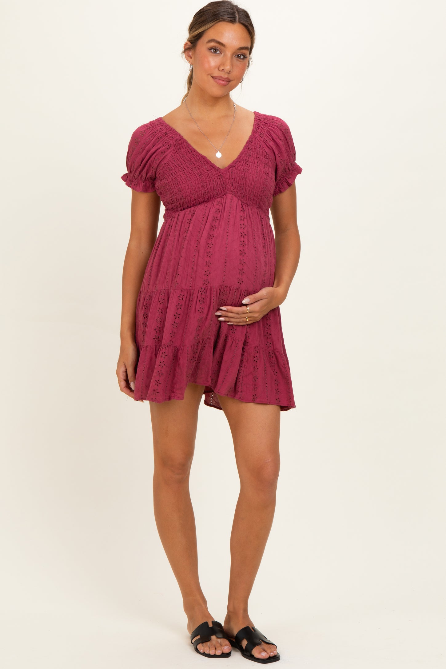 woman wearing a burgundy short sleeve maternity dress with a ruffled hem and holding her baby bump