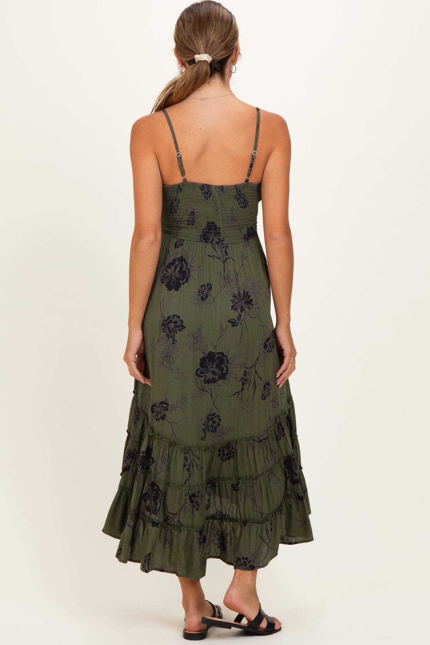 woman wearing a green floral maternity maxi dress with a tiered skirt and adjustable spaghetti straps, showing her back