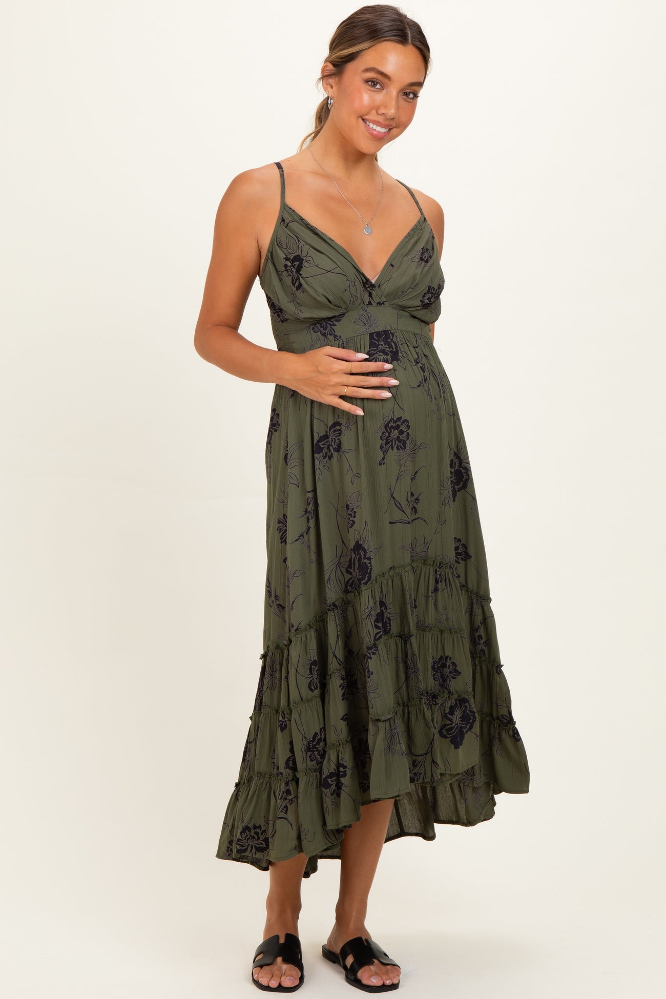 woman wearing a dark green floral print maternity maxi dress with a fitted bodice and tiered skirt, showing her baby bump