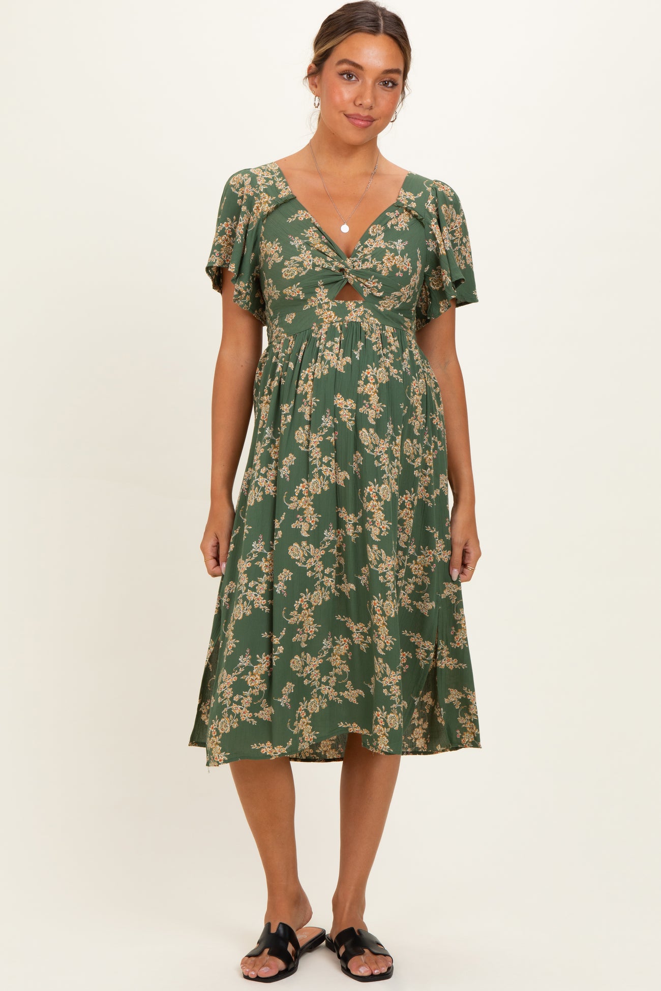 woman wearing a green floral print maternity dress with a deep V-neck and flutter sleeves, standing against a neutral background