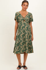 woman wearing a green floral print maternity dress with a deep V-neck and flutter sleeves, standing against a neutral background