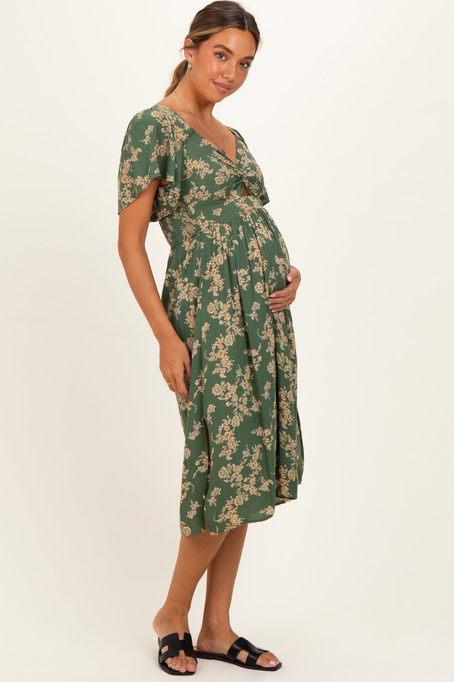 woman wearing a green floral maternity dress with short sleeves and a v-neck, holding her baby bump