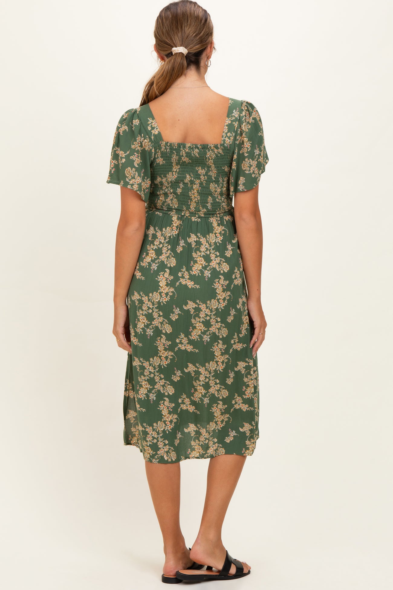 woman wearing a green floral maternity dress with short sleeves, showing the back view and gathered detailing