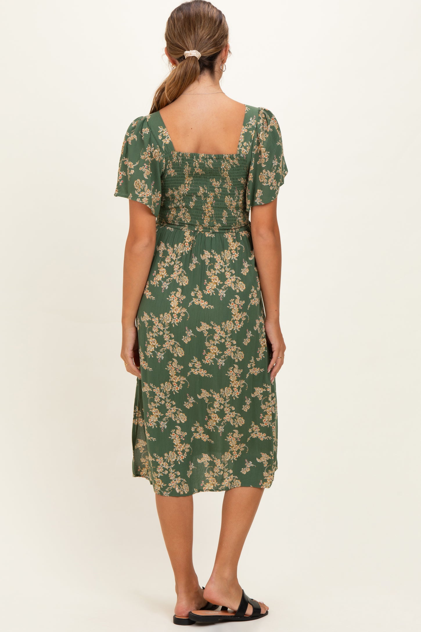 woman wearing a green floral maternity dress with short sleeves, showing the back view and gathered detailing