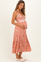 woman wearing a floral orange maternity dress with a baby bump, standing and holding her belly