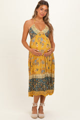 woman wearing a yellow floral maternity dress with a halter neckline and holding her baby bump