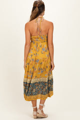 woman wearing a yellow floral maternity maxi dress with a halter neck and a flowing skirt, showing the back view