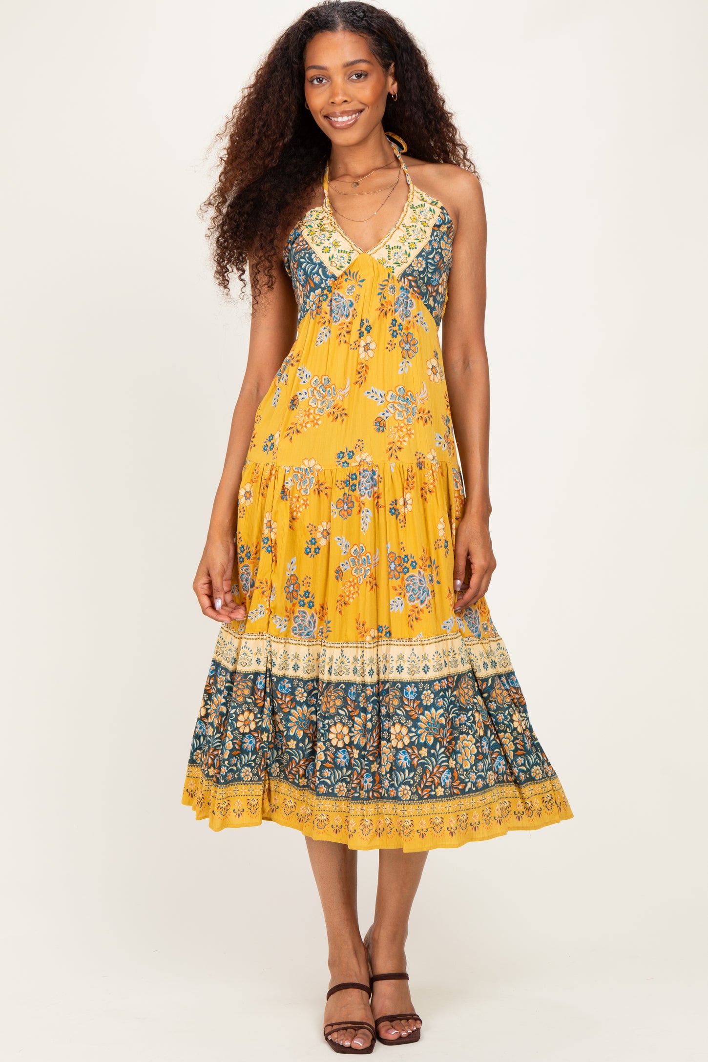 woman wearing a yellow floral halter neck maxi dress with tiered hem and intricate border details