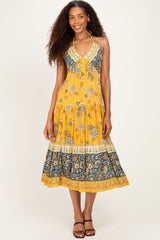 woman wearing a yellow floral halter neck maxi dress with tiered hem and intricate border details