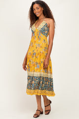woman wearing a yellow floral halter maxi dress with a tiered hem and intricate lace detailing