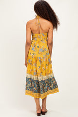 woman wearing a yellow floral maxi dress with a halter neckline and tiered skirt, viewed from the back