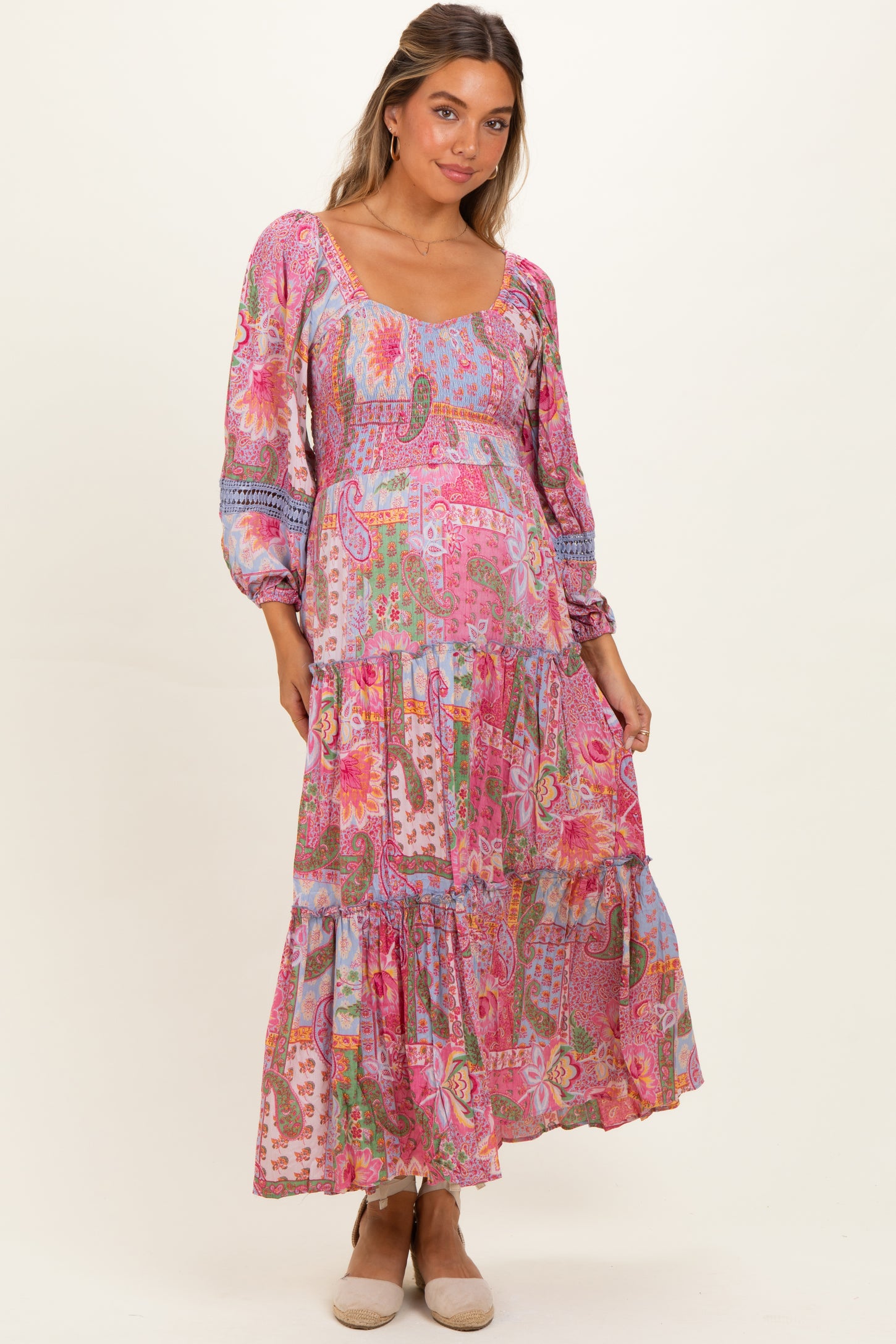 woman wearing a pink floral long sleeve maternity maxi dress with a tiered skirt and a visible baby bump