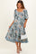 woman wearing a floral patterned maternity dress with a scooped neckline and tiered skirt, holding a small white bag