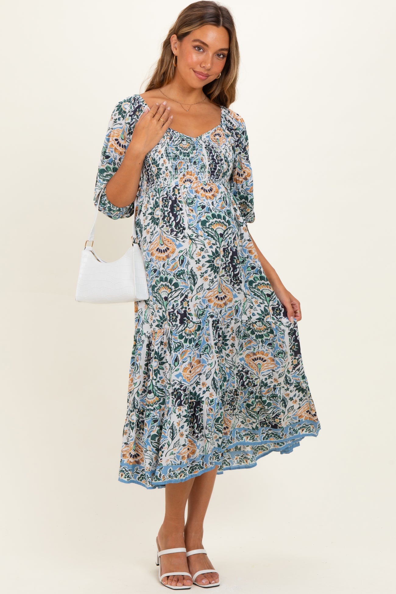 woman wearing a floral maternity dress with short sleeves and a flowing skirt, holding a white handbag