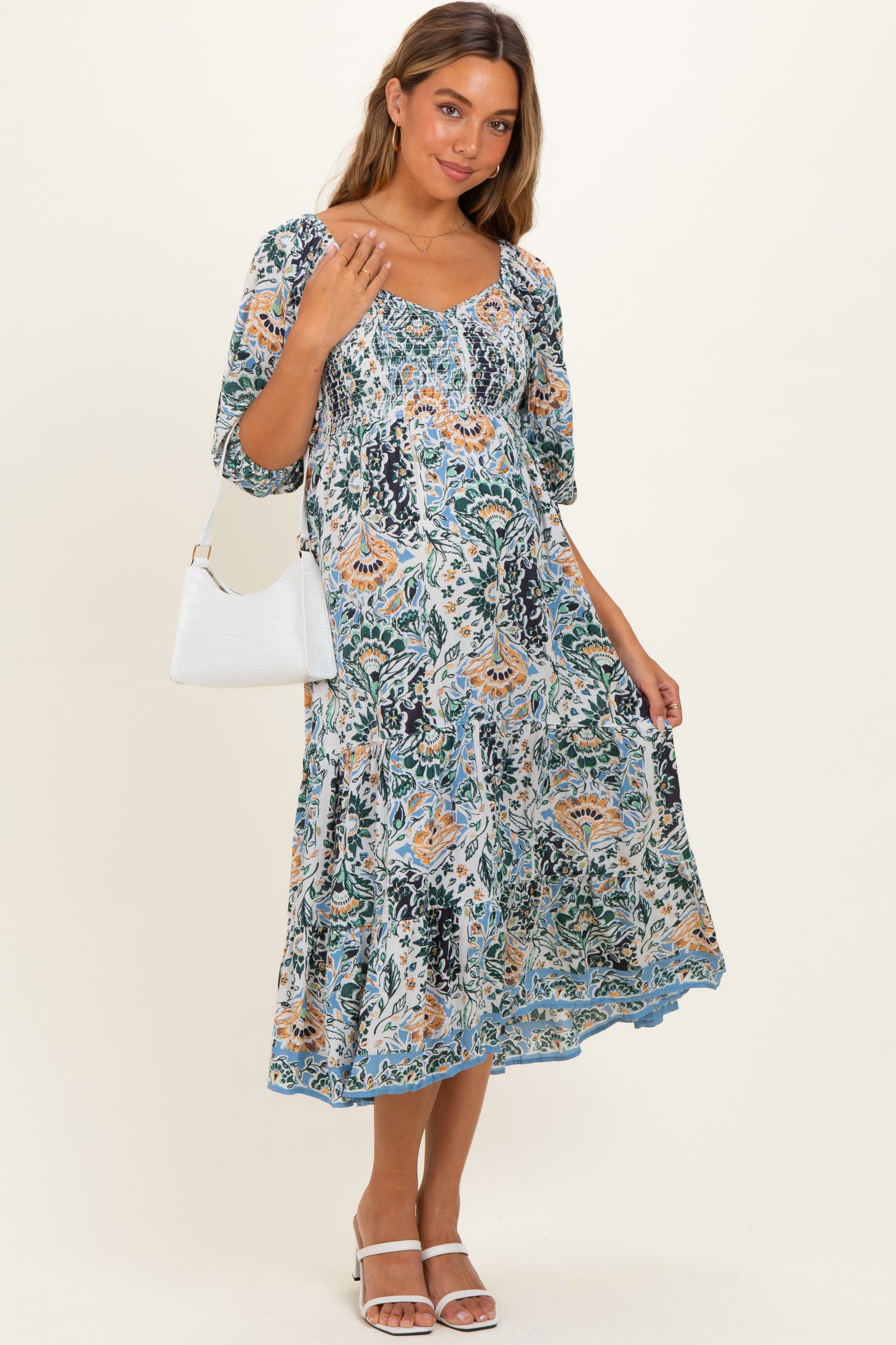 woman wearing a floral maternity dress with short sleeves and a flowing skirt, holding a white handbag