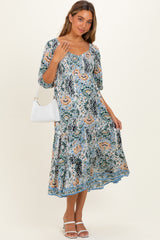 woman wearing a floral maternity dress with short sleeves and a flowing skirt, holding a white handbag