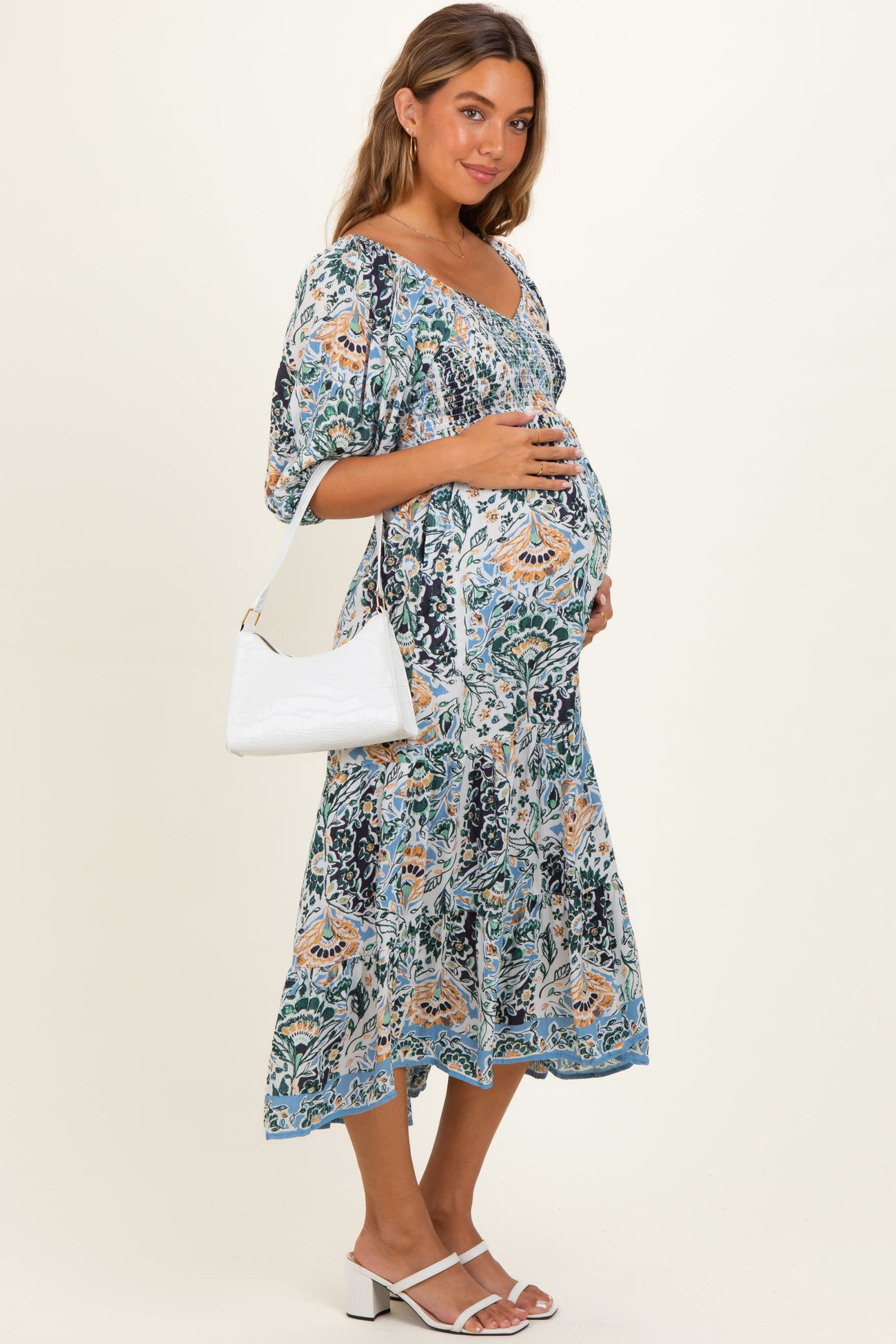 woman wearing a floral print maternity dress with a square neckline and a baby bump, holding a white handbag