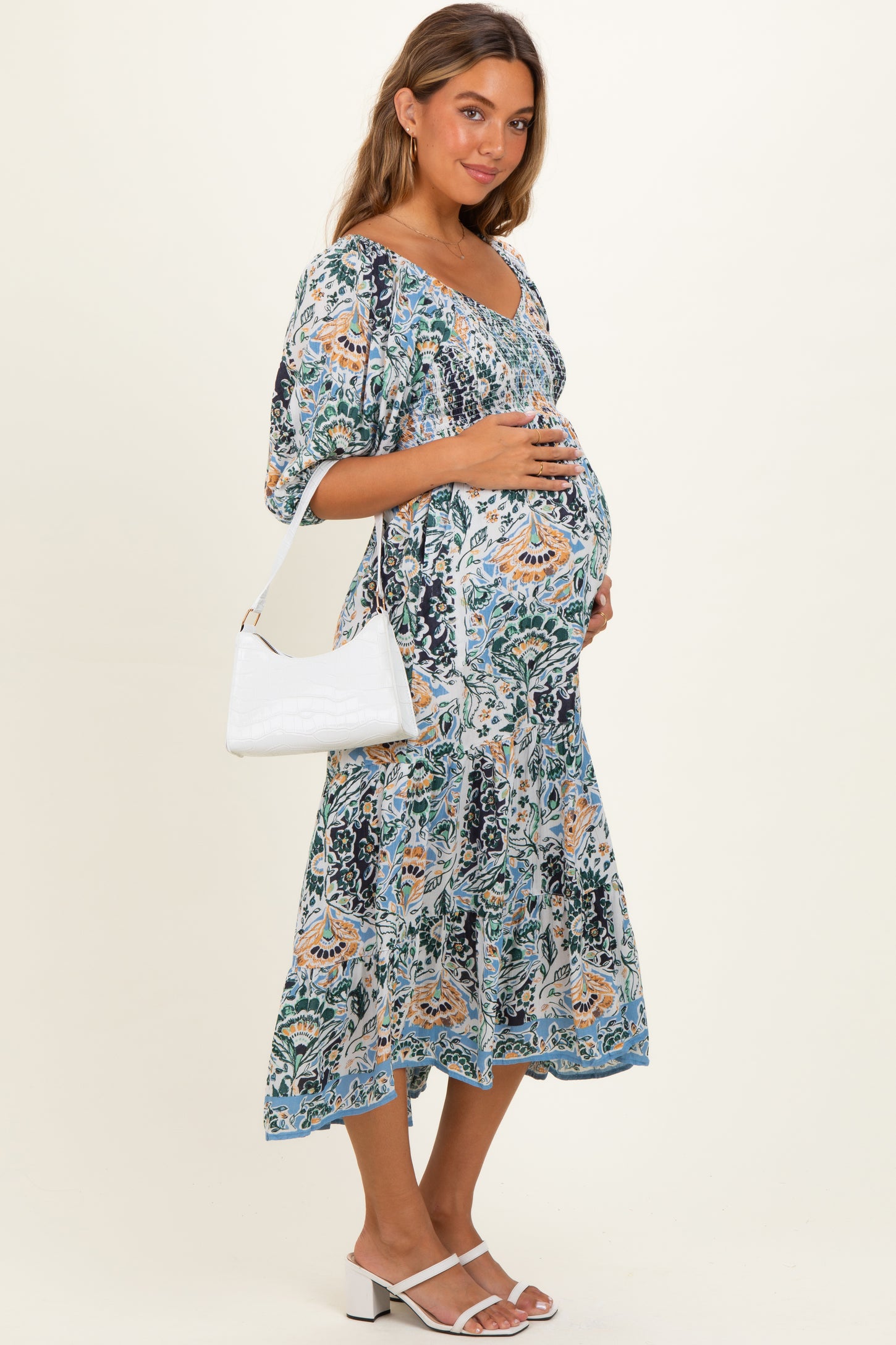 woman wearing a floral print maternity dress with a square neckline and a baby bump, holding a white handbag