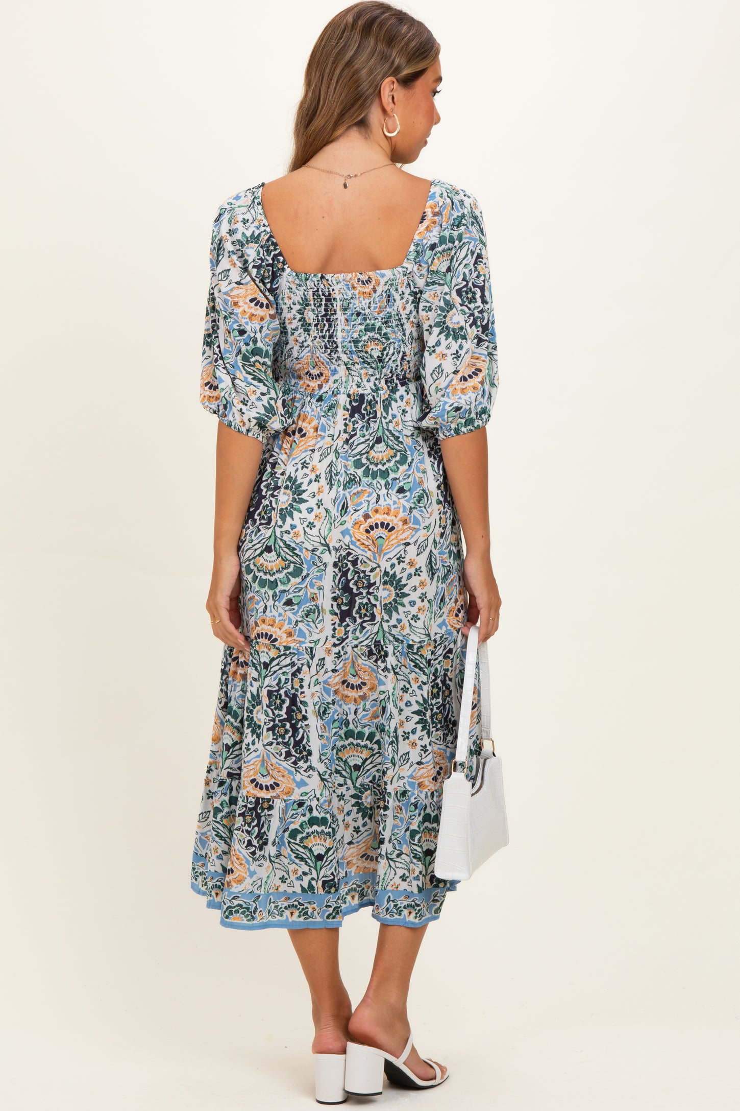 woman wearing a floral maternity maxi dress with a square neckline and puff sleeves, holding a small white handbag