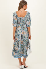 woman wearing a floral maternity maxi dress with a square neckline and puff sleeves, holding a small white handbag