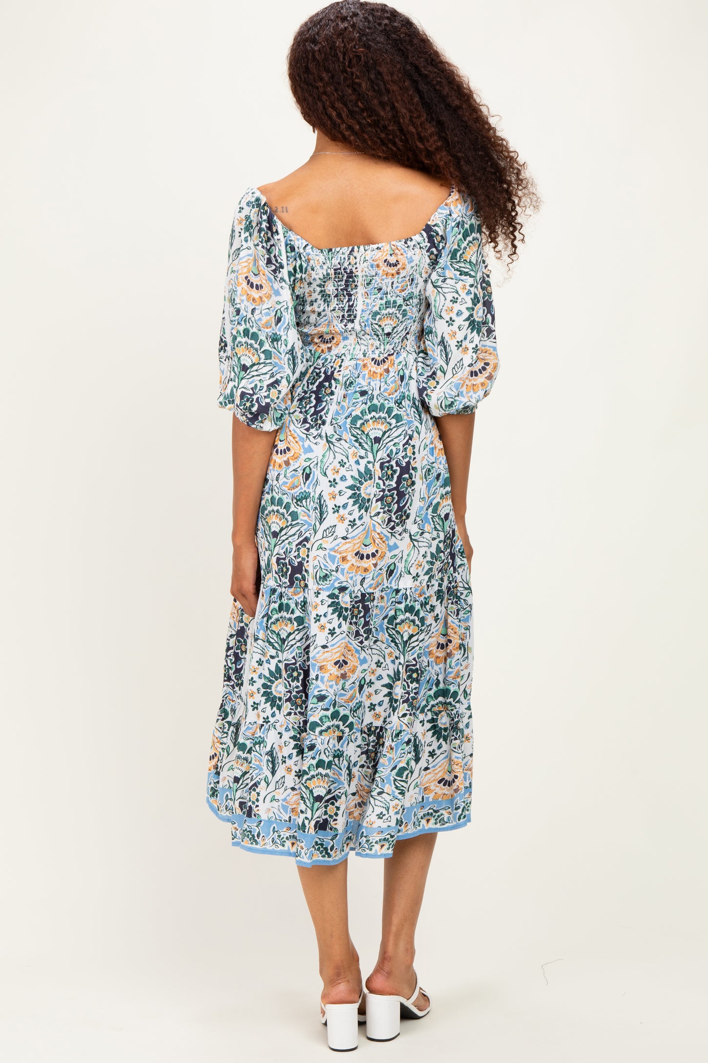 woman wearing a patterned midi dress with puff sleeves and a square back detail, standing with her back to the camera