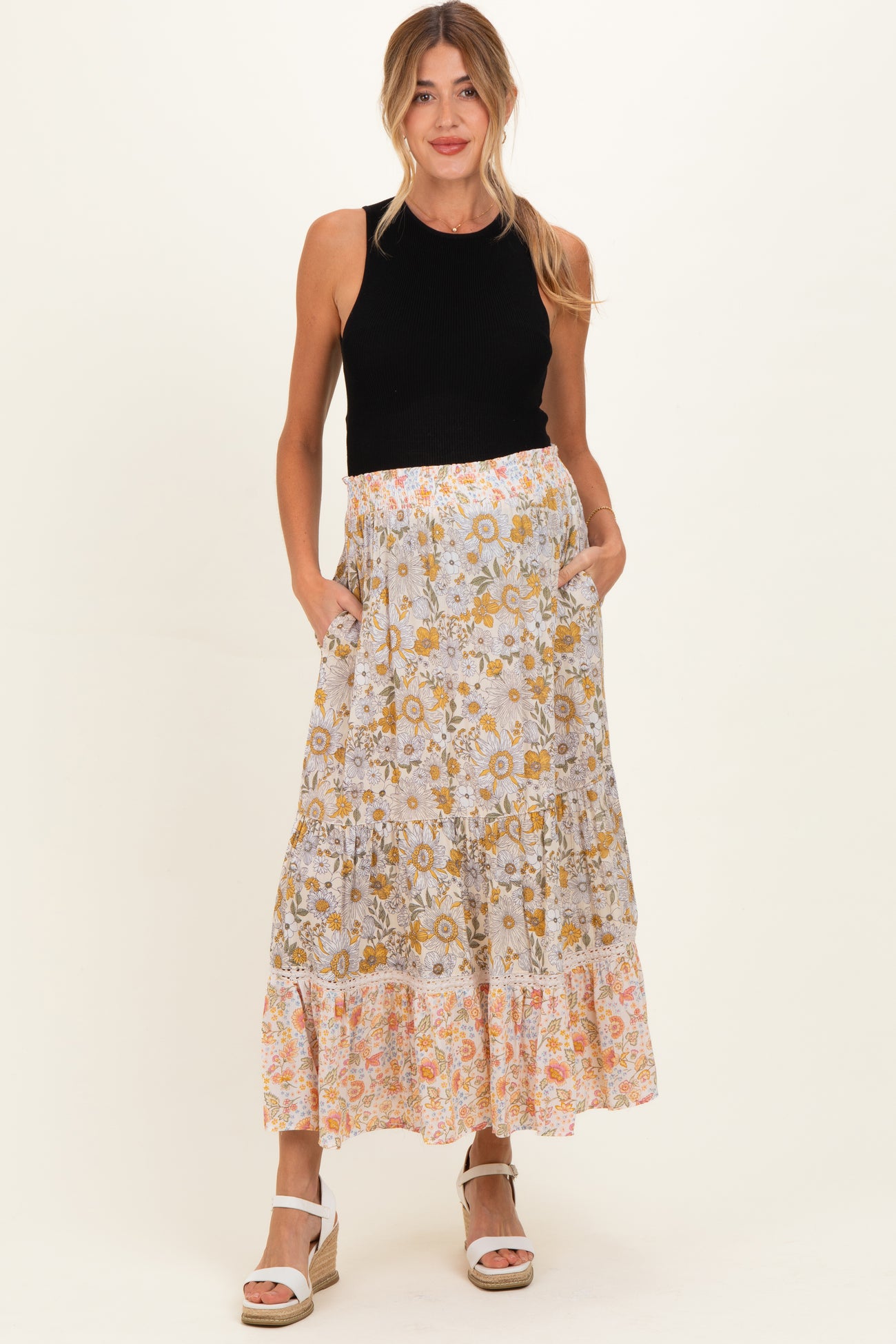 woman wearing a black sleeveless top and a patterned maternity skirt with pockets, standing and smiling