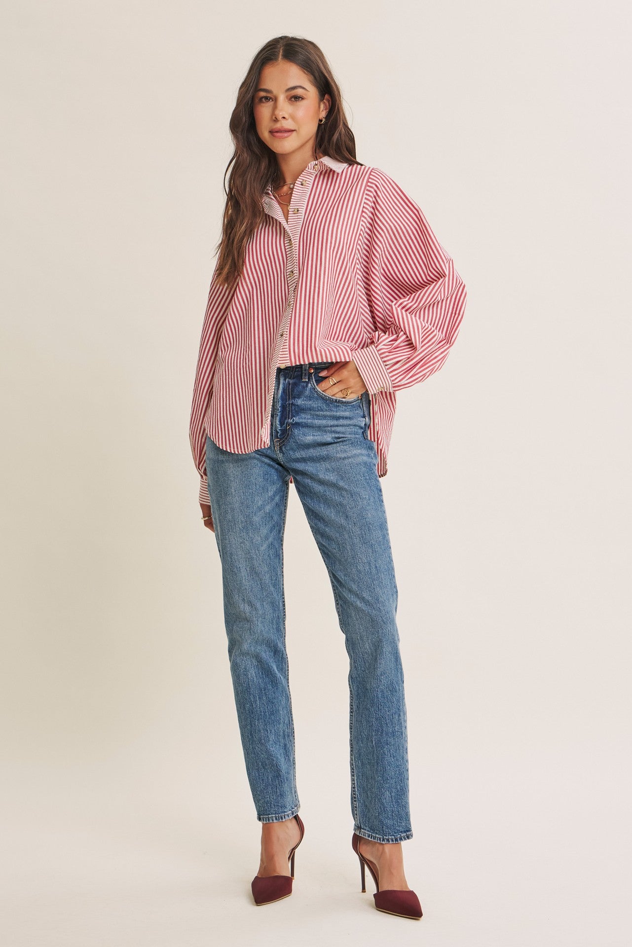woman wearing a red and white striped oversized button-up shirt with blue high-waisted jeans and burgundy heels