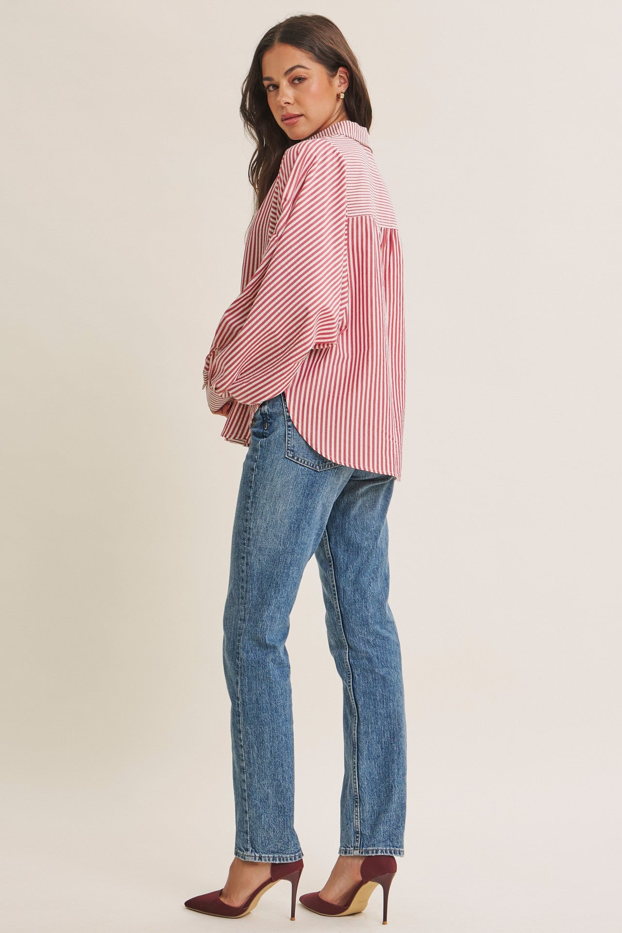 woman wearing a red and white striped oversized shirt with balloon sleeves and blue jeans, standing side view
