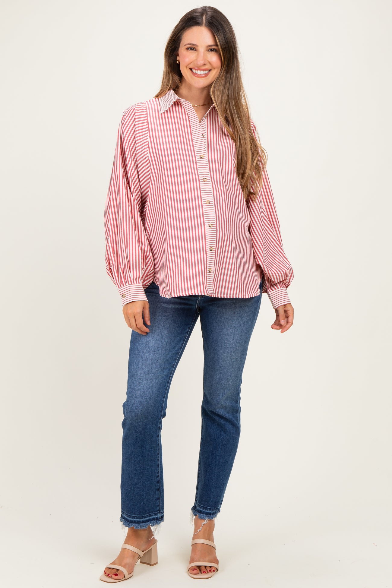 woman wearing a red and white striped maternity shirt with balloon sleeves and blue jeans, smiling at the camera
