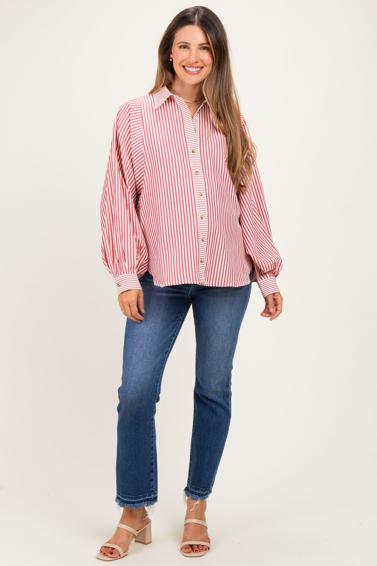 woman wearing a red and white striped maternity shirt with balloon sleeves and blue jeans, smiling at the camera