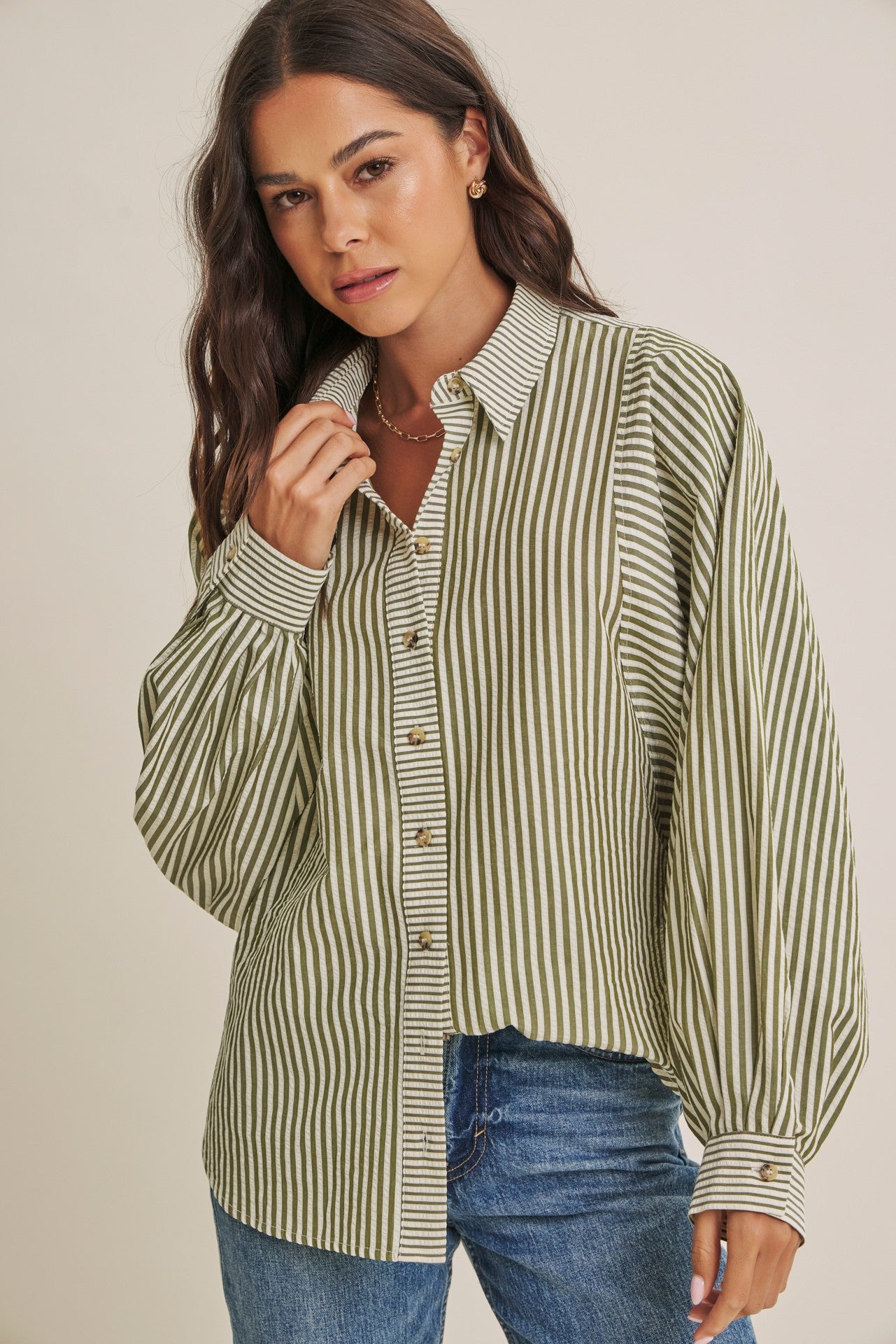 woman wearing a green and white striped oversized button-up shirt with puffed sleeves and paired with blue jeans