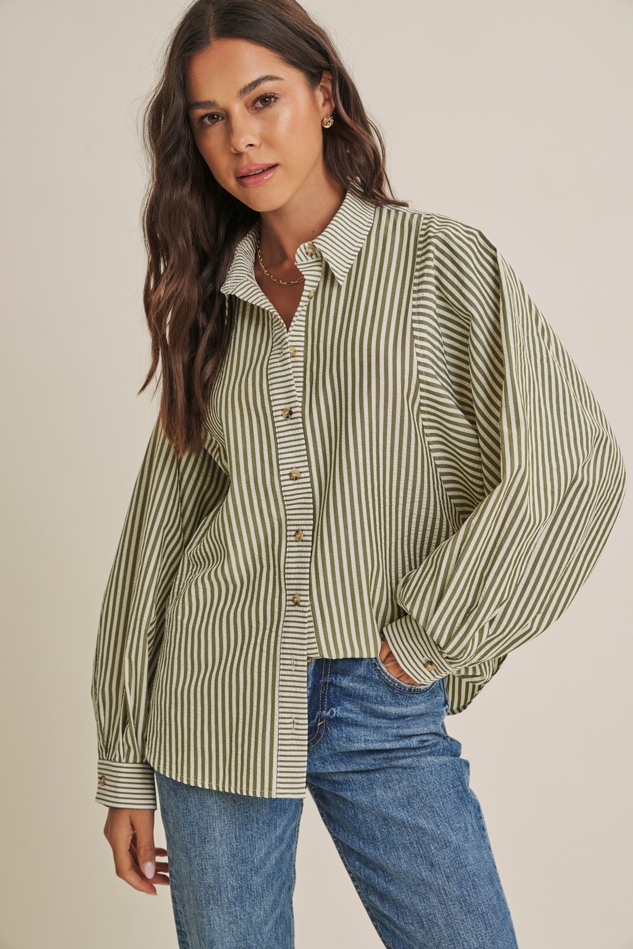 woman wearing a green and white striped oversized button-up shirt with rolled sleeves and light blue jeans